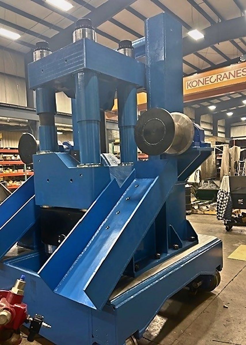 Tall blue machine stand with guide rolls and angled chutes, built in house